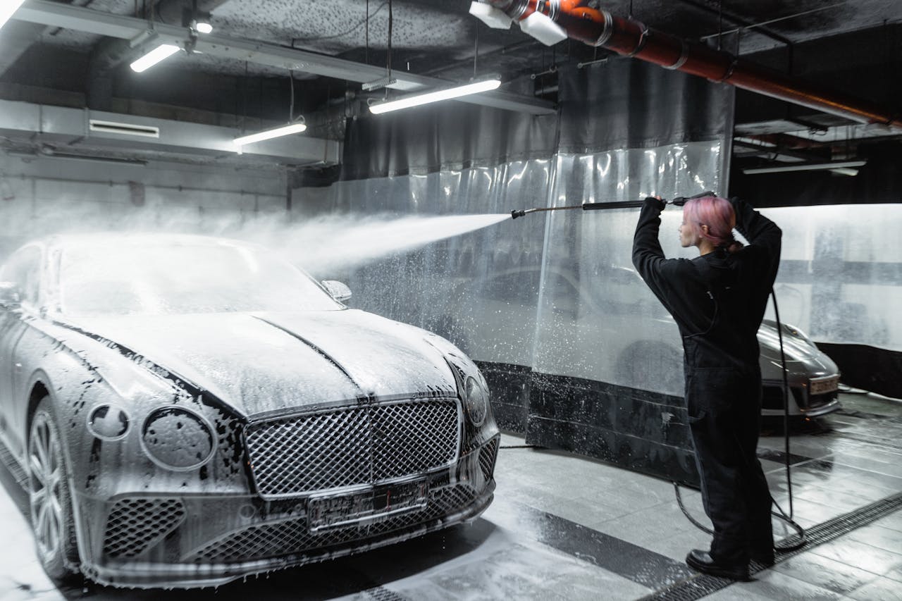 A woman expertly cleans a car using snow foam in a modern indoor car wash facility.