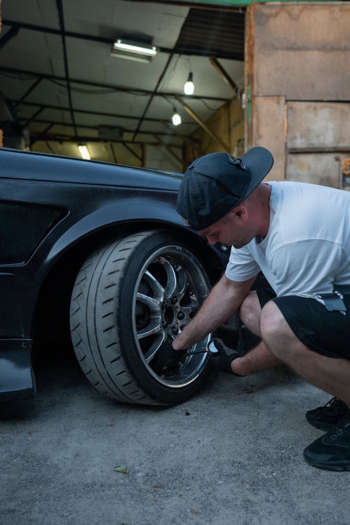 A man changes a car tire in a garage workshop, showcasing automotive maintenance.